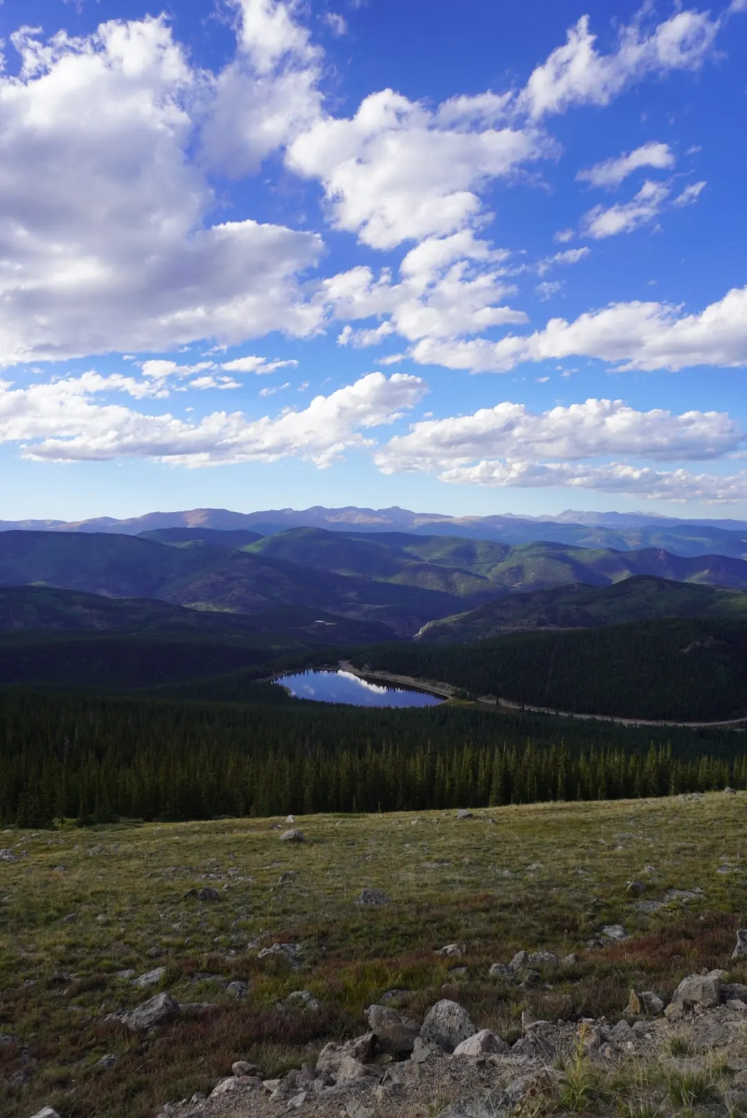 A small lake below forested ridges under a sky full of white clouds.